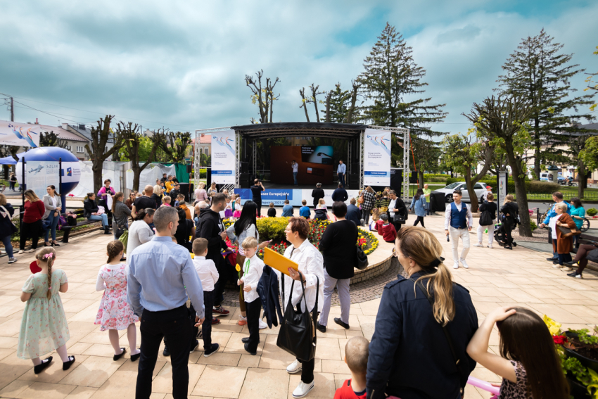 Grupa ludzi stoi przed zadaszoną sceną. Po lewej stronie znajduje się balon reklamowy.