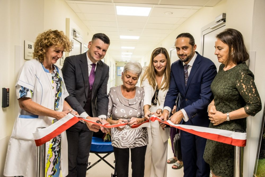 4 kobiety i 2óch mężczyzn przecinają wstęgę na znak otwarcia nowego oddziału szpitalnego. Wszyscy są uśmiechnięci..
