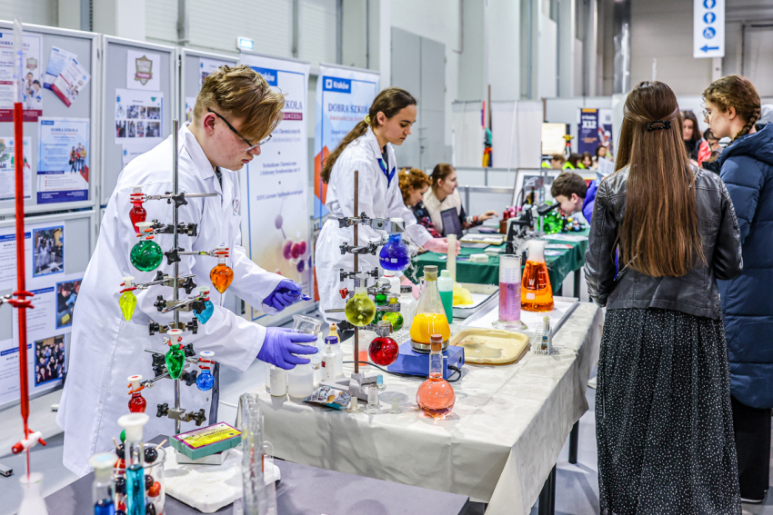 Stoisko chemiczne, przy którym chlopak idziewczyna prezentują doświadczenia chemiczne.