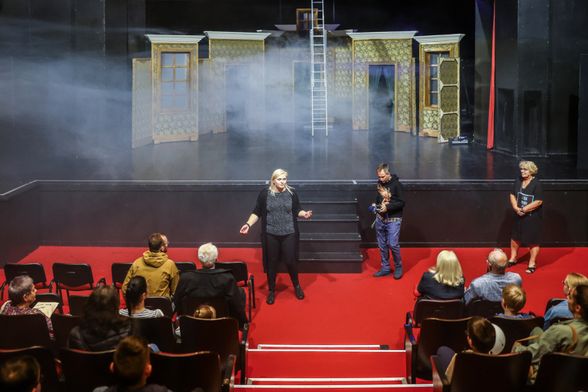 Scena teatralna. Na widowni siedzący ludzie.
