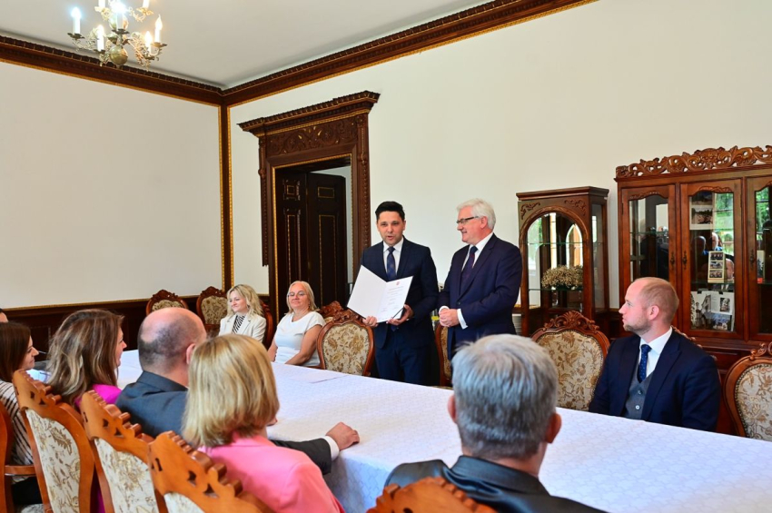 Grupa osób przy stole konferencyjnym, w eleganckiej sali.