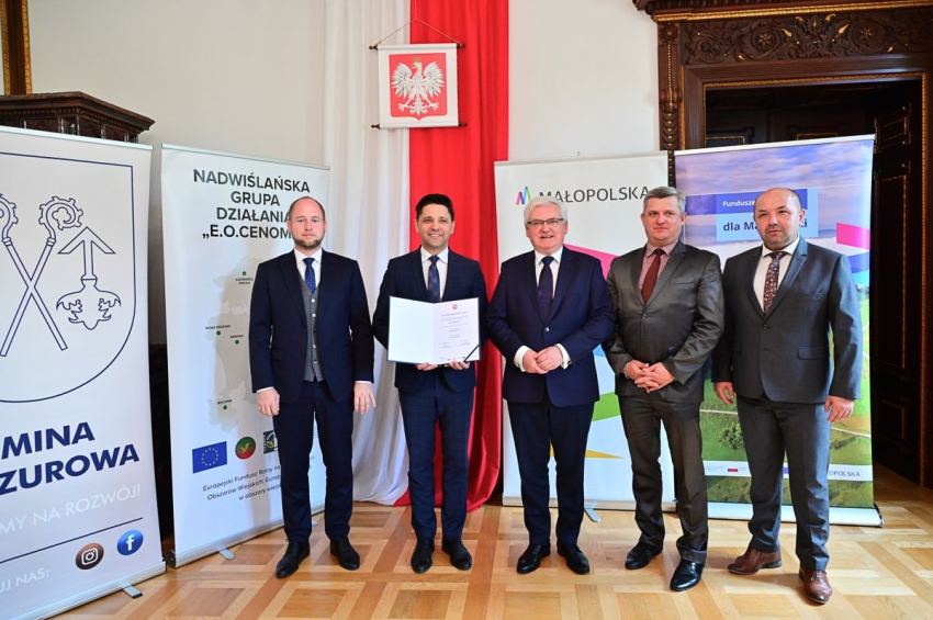 Pięciu mężczyzn w garniturach stoi w eleganckiej sali . jeden z znich trzyma dokument-promesę.