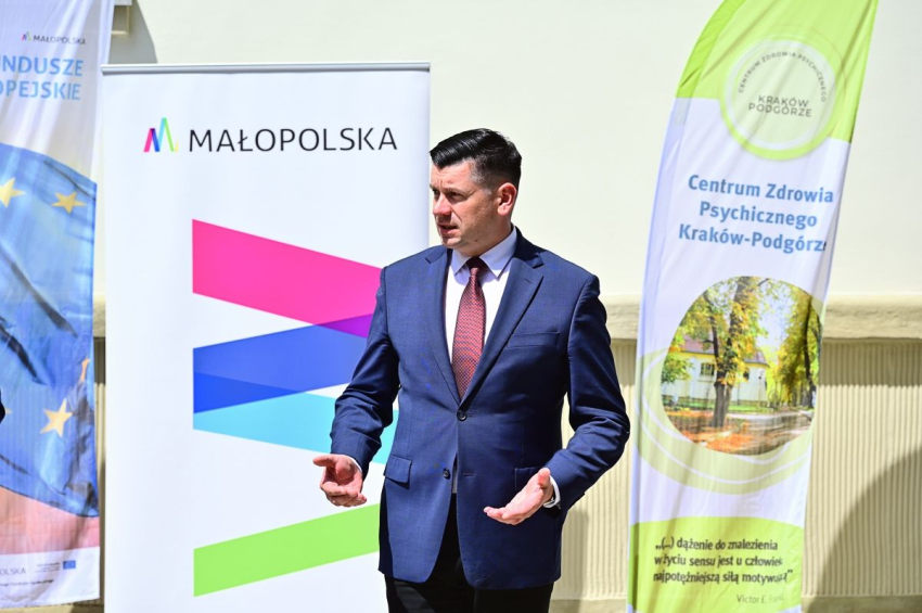 Mężczyzna w garniturze przemawia przed budynkiem.