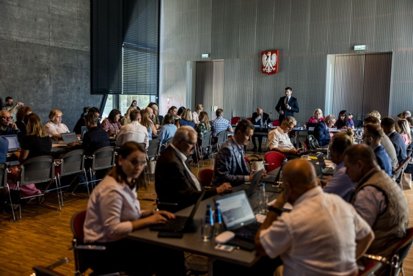 Członkowie posiedzenia przy stołach konferencyjnych.