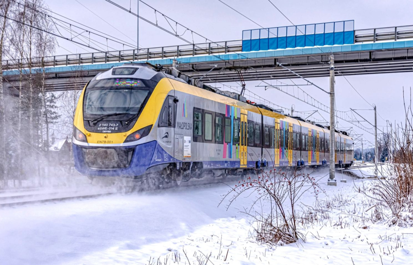Pociąg przejeżdżający pod wiaduktem zimą.