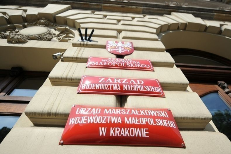 Czerwone tablice informacyjne na ścianie bundy informujące że znajduje się w nim Urząd Marszałkowski Województwa Małoplskiego w Krakowie, Zarząd Województwa Małopolskiego oraz Sejmik Województwa Małopolskiego.