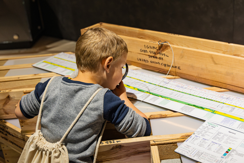 Chłopiec pochyla się nad wykresem i ogląda go przez szkło powiększające.
