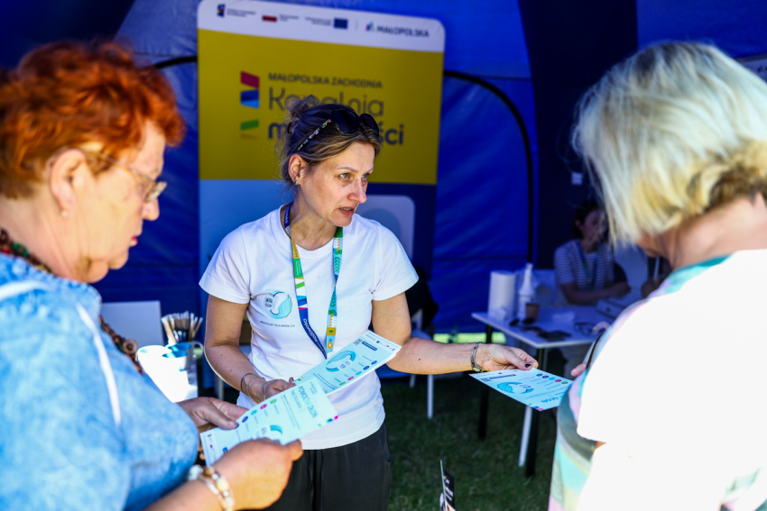 Kobieta daje ulotki informacyjne uczestnikom wydarzenia.