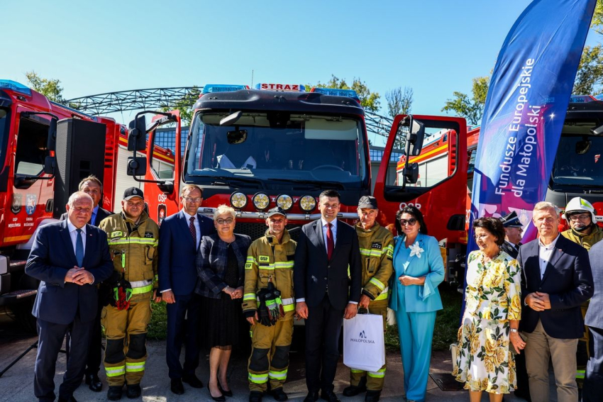 Zdjęcie grupowe uczestników wydarzenia na tle samochodu strażackiego.
