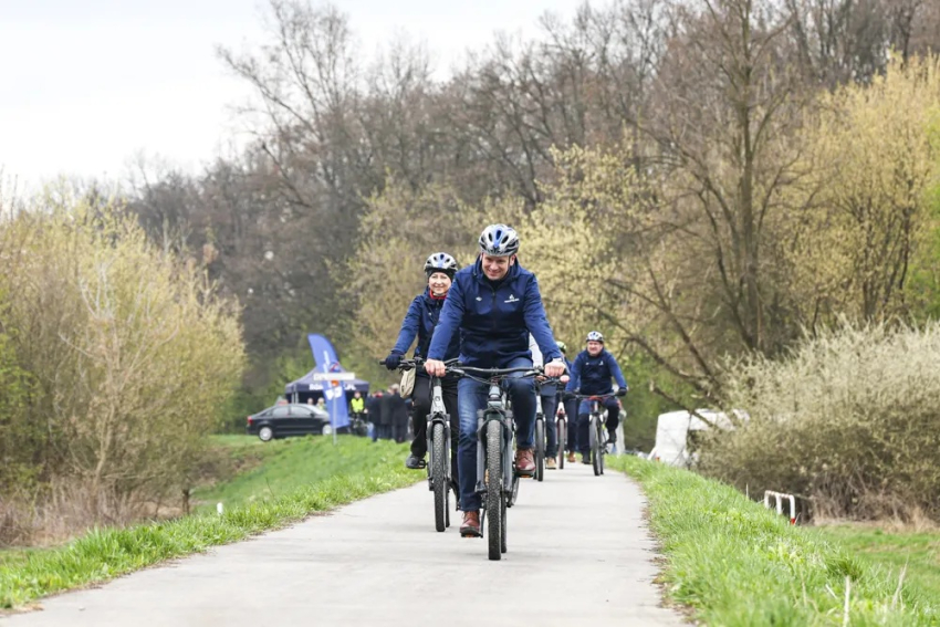 Kilka osób jedzie na rowerach po asfaltowej ścieżce wśród zieleni