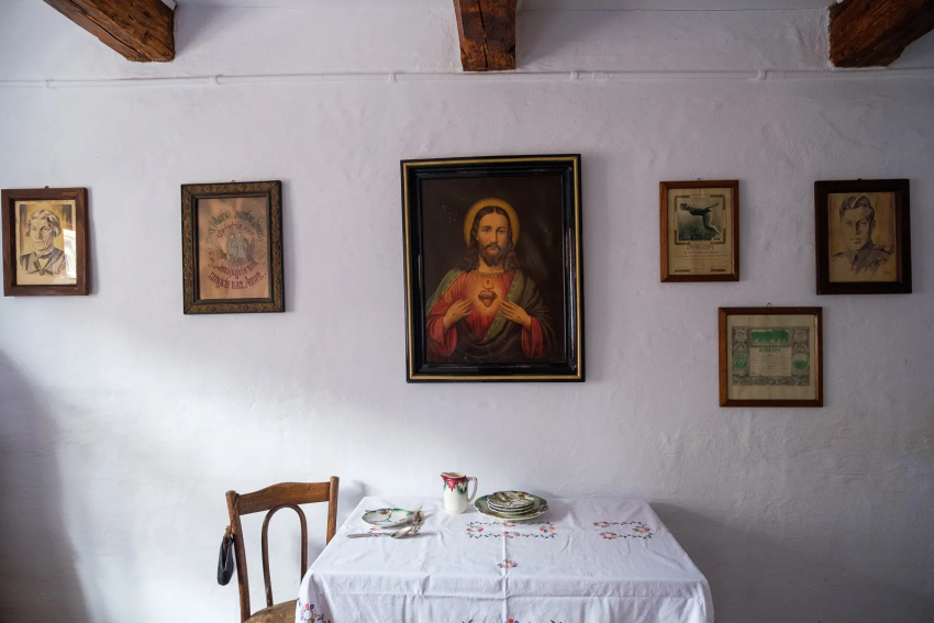 Wnętrze chaty. Stół z nakryciem. Na ścianie obraz Jezusa i fotografie przedstawiające mężczyz.