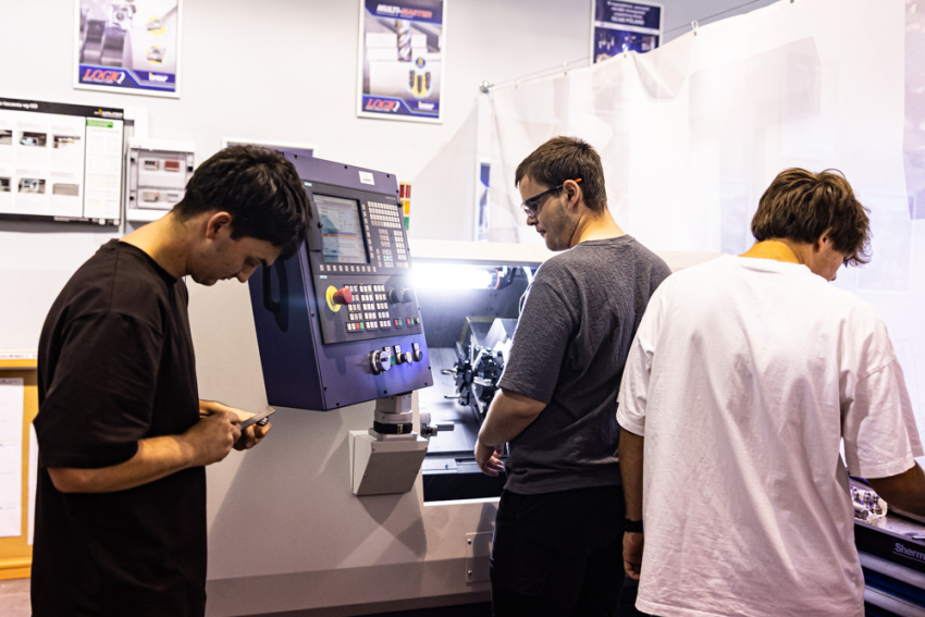 Trzech uczniów podczas zajęć praktycznych przy obrabiarce CNC w szkolnej pracowni technicznej