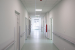 Zdjęcie przedstawia szpitalny korytarz z białymi ścianami i jasną podłogą