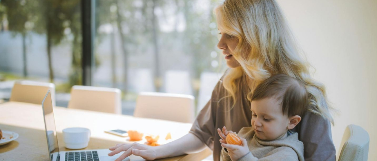 Mama pracująca przy laptopie siedzi z synkiem na kolanach