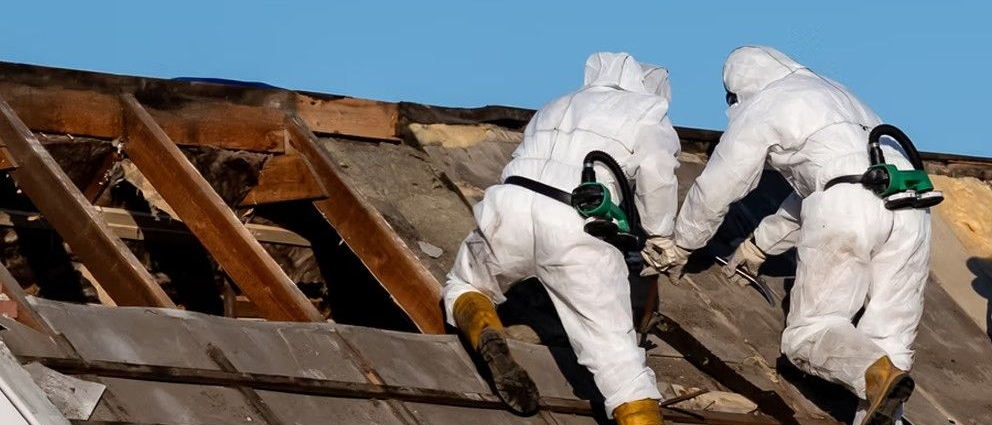 Robotnicy w kombinezonach ochronnych usuwają azbest z dachu.