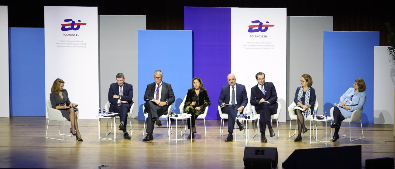 Osiem osób siedzących na krzesłach ustawionych obok siebie na scenie. W głębi kolorowe plasze z logotypem Polskiej prezydencji w Unii Eropejskiej w 2025 roku oraz adresem strony internetowej Poland25.EU
