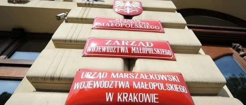 Czerwone tablice informacyjne na ścianie bundy informujące że znajduje się w nim Urząd Marszałkowski Województwa Małoplskiego w Krakowie, Zarząd Województwa Małopolskiego oraz Sejmik Województwa Małopolskiego.