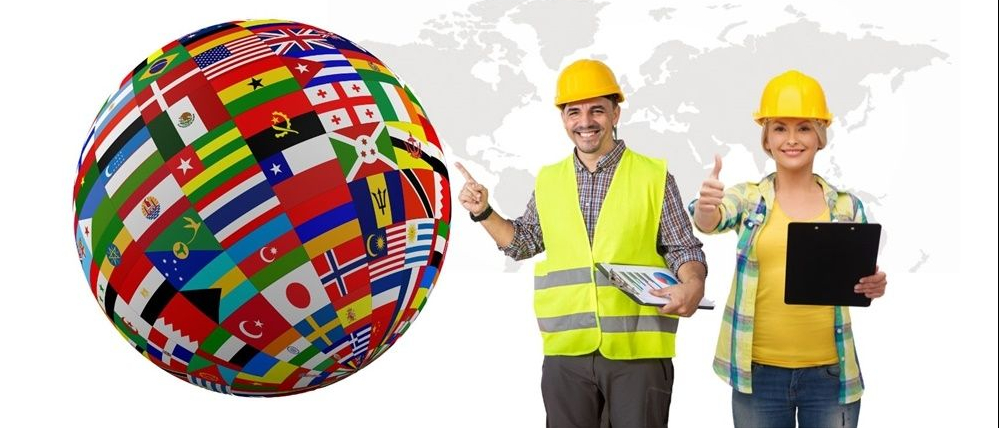 Kobieta i mężczyzna w żółtych hełmach roboczych wskazują na globus z flagami różnych krajów.