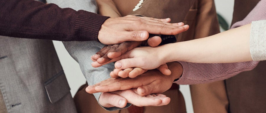 Dłonie kilku osób złożone jedne na drugich.