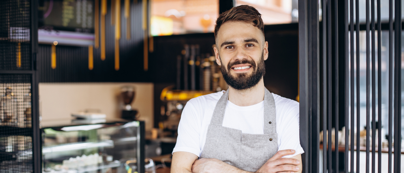 Młody mężczyzna w fartuchu barmana stoi w drzwiach kawiarni.