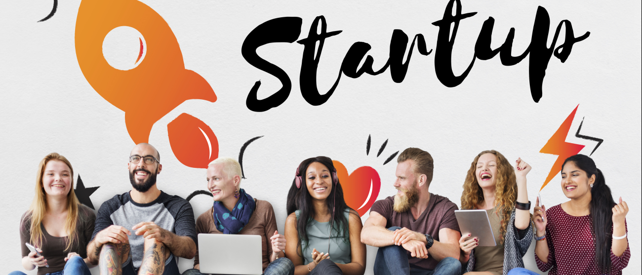 Młodzi ludzie siedzą przy ścianie z napisem Startup.