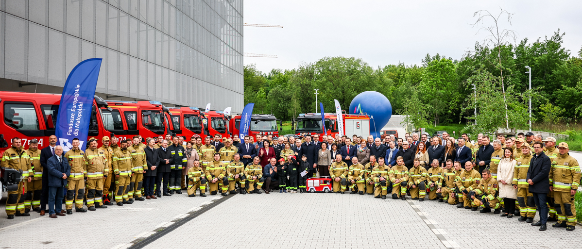 Zdjęcie grupowe uczestników wydarzenia. Za nimi samochody strażackie.